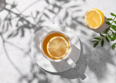 Beyaz bir masada limonlu ve yeşil dallı bir fincan çay. Kahvaltı detoksu ve sağlıklı konsept. Üst görünüm ve kopyalama alanı.