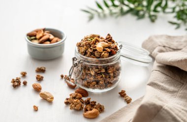Beyaz arka planda fındıklı ve peçeteli kavanozda ev yapımı granola. Rahatlatıcı yemek. Kahvaltıda sağlıklı ve besleyici tahıl müsli konsepti.. 