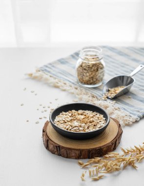 Tabaktaki yulaf ezmesi ve mutfak penceresinin önündeki beyaz desenli masada peçetedeki kavanozda. Sağlıklı bir kahvaltı hazırlamak için doğal vegan mısır gevreği ürünü konsepti. Boşluğu kopyala.