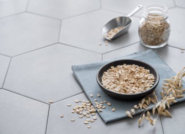 Tabaktaki yulaf ezmesi ve gri beton bir fayansta peçetedeki kavanozda. Sağlıklı bir kahvaltı hazırlamak için doğal vegan mısır gevreği ürünü konsepti. Boşluğu kopyala.