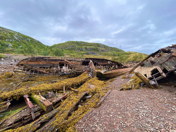 Старые деревянные руины корабля на скалистом побережье, природный стиль, облачное небо, концепция заброшенности и распада в природной среде. Териберка, Россия.