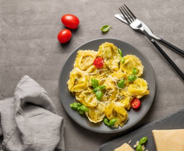 Parmesanlı Tortellini makarna, pesto ve fesleğen peynirli, çatal bıçaklı ve domatesli koyu bir tabakta. Geleneksel İtalyan ev yapımı yemek konsepti. Üst görünüm, alanı kopyala.