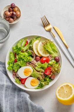 Kiraz domatesli ton balığı salatası, yumurta, zeytin ve salatalık beyaz bir tabakta limon, peçete ve çatal bıçakla birlikte. Sağlıklı Akdeniz yemekleri konsepti. Üst görünüm, alanı kopyala.