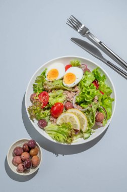 Kiraz domatesli ton balığı salatası, yumurta, zeytin ve salatalık. Mavi arka planda, çatal bıçaklı. Reklam menüsü kafesi için sağlıklı Akdeniz yemekleri konsepti. Üst görünüm, alanı kopyala.