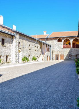 Tarihsel taş manastır avlusunda parlak, berrak gökyüzü altında gerçekçi şekillerde kemerli freskler var. Miras ve sükunet kavramı. Kıbrıs.
