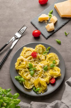 Parmesanlı Tortellini makarna, pesto ve fesleğen peynirli, otlu ve domatesli koyu bir tabakta. Geleneksel İtalyan ev yapımı yemek konsepti. Üst görünüm, alanı kopyala.