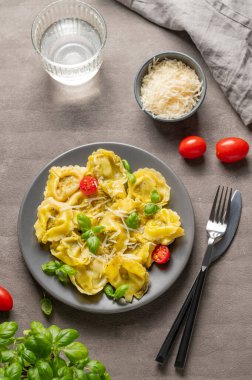 Parmesanlı Tortellini makarnası, pesto ve fesleğen bir tabakta bir bardak su, peynir, bitki ve domates ile birlikte. Geleneksel İtalyan ev yapımı yemek konsepti. Üst görünüm.