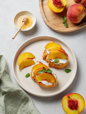 Şeftali, nektarin, krem peynir ya da ricotta ve ballı tost bruschetta taze meyve ve nane ile hafif bir arka planda. Sağlıklı yaz atıştırmalığı konsepti. Üst görünüm, alanı kopyala.