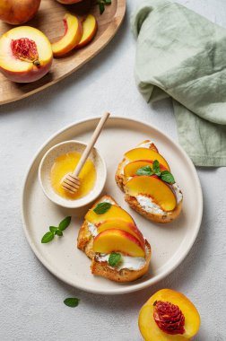 Şeftali, nektarin, krem peynir ya da ricotta ve ballı kızarmış bruschetta taze meyve ve peçeteyle hafif bir arka planda. Sağlıklı yaz atıştırmalığı konsepti. Üst görünüm, alanı kopyala.