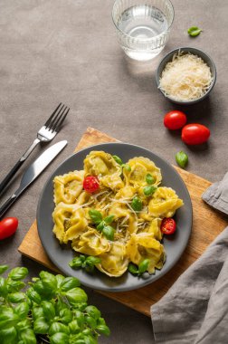 Parmesanlı Tortellini makarnası, pesto ve fesleğen bir tabakta bir bardak su, peynir, bitki ve domates ile birlikte. Geleneksel İtalyan ev yapımı yemek konsepti. Üst görünüm, alanı kopyala.