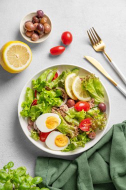 Kiraz domatesli ton balığı salatası, yumurta, zeytin ve salatalık beyaz bir tabakta limon ve çatal bıçakla birlikte. Sağlıklı Akdeniz yemekleri konsepti. Üst görünüm, alanı kopyala.