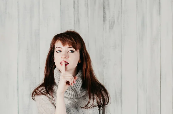Hush. View of seductive woman asking for silence, quiet or secrecy with finger on lips, looking sideway. Shh hand gesture, light background wall. Pretty girl placing finger on lips with shhh sign symbol. Emotion facial expression, body language