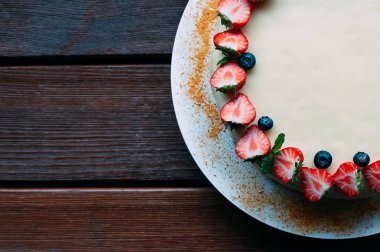 Taze çilek, yaban mersini ve nane, kahverengi ahşap masa arka plan üzerinde beyaz buzlanma ile lezzetli pasta süslenmiş. Görüntü menüsü veya şekerleme kataloğu için. Üstten görünüm