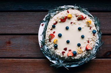 Lezzetli pasta beyaz çikolata sosu ile taze çilek, yaban mersini, goji, limon ve biberiye, kahverengi ahşap masa arka plan ile dekore edilmiştir. Üstten görünüm görüntü menü veya şekerleme kataloğu için