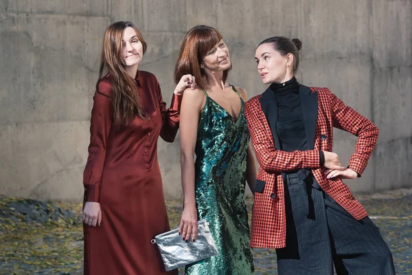 Street style Fashion portrait three charming women. Brown and green dress, Black, tile red jacket, silver bag. Summer Spring Fall collection beautiful look. Togetherness, friendship, party concept