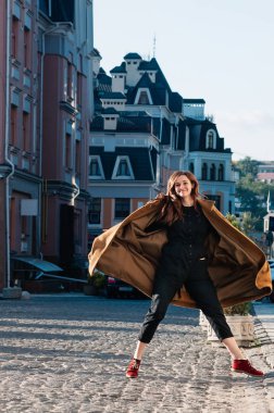 Şirin mutlu kadın model şık siyah tulum ve sarı ceket cadde, şehir arka plan, ilkbahar veya sonbaharda atlama tam uzunlukta vurdu. Hareket Bulanıklığı görüntü. Eğlenceli yaşam tarzı mutluluk kavramı