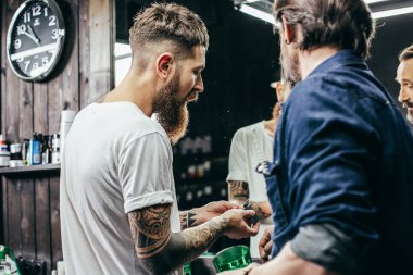 Birbirine yakın duran ve yeni saç kesme bıçaklarına bakan iki sakallı berberin yakın