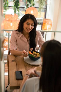 Bir kafede öğle yemeği sırasında bir çatal tutarken bir gülümseme ile arkadaşına bakarak mutlu genç kadın