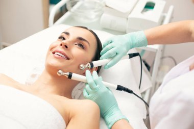 Cildine dokunan ve gülümseyen özel prongs ile mikrocurrent tedavi gören hevesli genç bayan