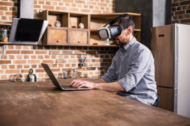 Meşgul işçi. Vr cihazını kullanırken dizüstü bilgisayar üzerinde çalışan konsantre işadamı