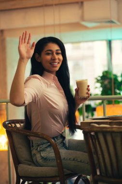 Rahat giysiler içinde Dost koyu saçlı bayan bir el koyarak ve bir bardak latte ile otururken gülümseyerek ve mesafe içine bakarak