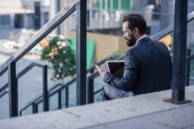 Günlük iş. Dizüstü bilgisayarını ve akıllı telefonlarını açık havada kullanan profesyonel bir işadamının arka görünümü