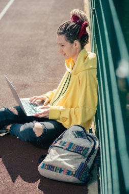 Spor sahasında dizüstü bilgisayarıyla otururken kendinden emin görünen dreadlocks ile sakin genç bayan
