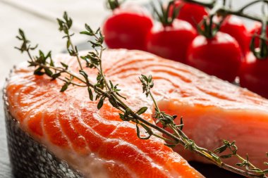 Üzerinde taze kekik dalı ve arka planda yatan kiraz domates ile pişmemiş kırmızı somon dilimi yakın