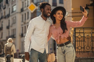 Sokakta duran siyah şapkalı güzel bayan gülümseyen ve onunla selfie çekerken arkadaşına sarılarak