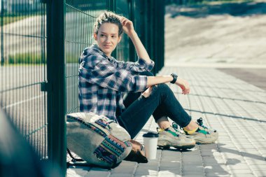 Zincir bağlantı çit yanında otururken gülümseyen ve spor zemin bakarak korkunç kilitleri ile Sakin genç kadın