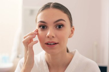 İlgilenen ve gözlerinin açık olması ve göz altındaki dereye dikkatlice dokunması ile yakından ilgilenen genç kadının yakın