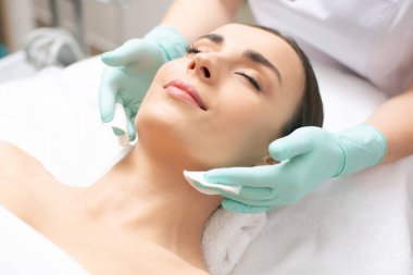 Sakin genç kadın kapalı gözlerle yatan ve gülümseyen elleri lastik eldiven boynuna yakın pamuk pedleri tutan iken