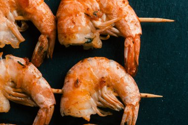 Siyah kayrak arka plan üzerinde ahşap şişler üzerinde dört kızarmış karides yakın