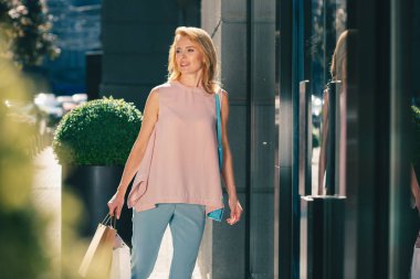 Sakin gülümseyen bayan alışverişten sonra elinde kağıt torbalar ile yürüyüş