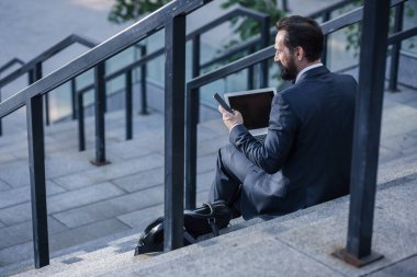 İletişime geçin. Akıllı telefonlarını kullanırken merdivenlerde oturan hoş profesyonel işadamı