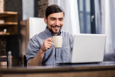 İyi bir ruh halinde. Onun laptop kullanırken kahve içme neşeli genç adam