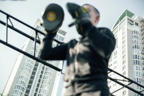 Waist up of the professional trainer wearing focus mitts while standing against the skyscrapers