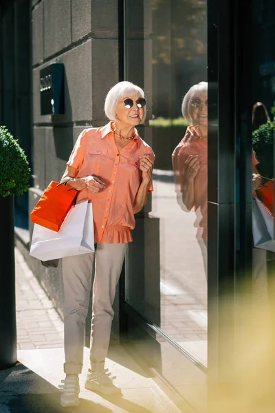 Senhora sorridente com sacos de compras perto da janela de vidro — Fotografia de Stock