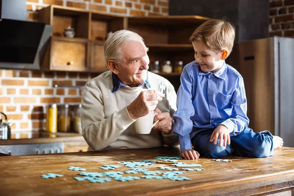 发展你的技能 快乐的老人微笑着和他的小孙子组装拼图 — 图库照片