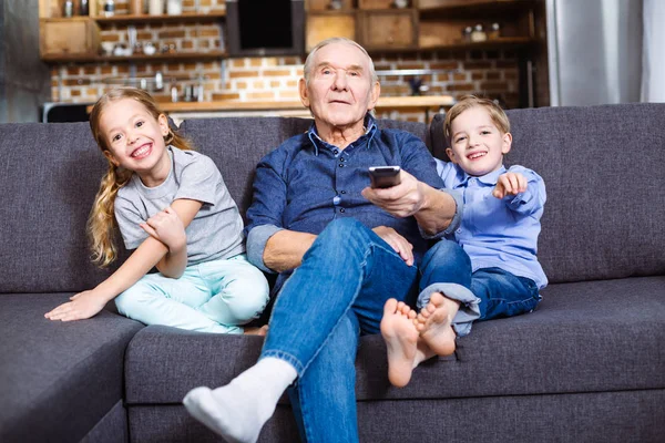 懒惰的休息 愉快的老人拿着遥控器 一边看电视 与他的孙子 — 图库照片