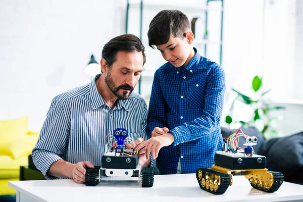 微笑的聪明的男孩展示一个机器人设备 而休息与他的儿子在家里 — 图库照片
