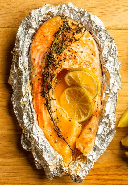 Top view image of the delicious fish slice baked in foil with thyme branch and slices on lime on the top