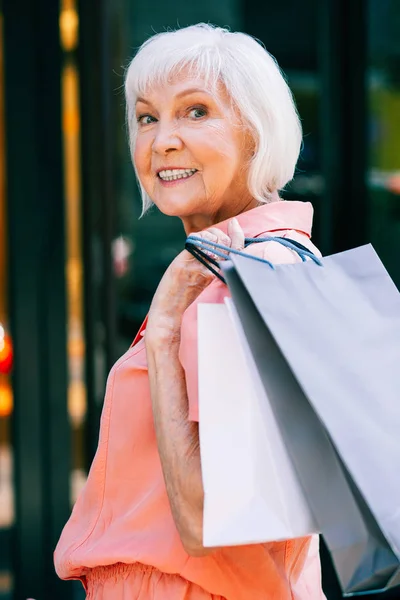 Positive elderly woman with shopping bags turning and smiling