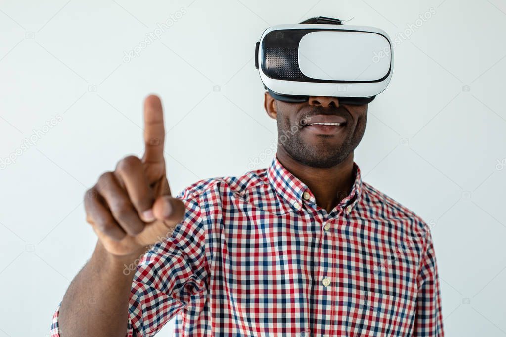 Touchable gadget. Pleasant smiling afro american man wearing VR glasses while standing against white background