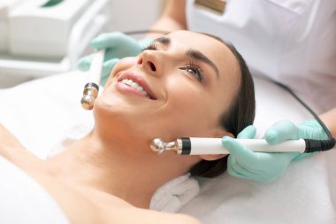 Rahat genç kadın iyi duygu ve metal uçlu ile mikrocurrent tedavi sırasında gülümseyen