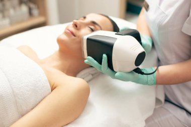 Genç bayanın cilt durumunu analiz eden taşınabilir aletin yakın çekim