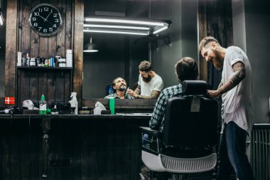 Professional friendly barber smiling and looking attentive while combing the beard of his client