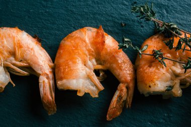 Siyah kayrak yüzeyinde lezzetli başsız kızarmış karides üst görünümü. Karidesler üzerinde kekik sprig