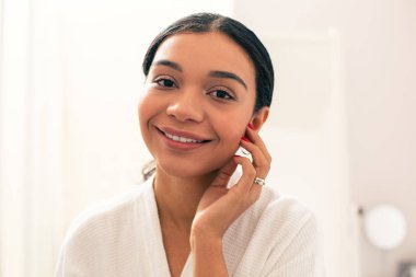 Bir eliyle yanağını dokunarak ayakta ve gülümseyen güzel genç kadın yakın