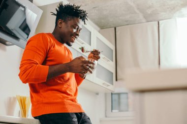 Kırmızı kazak neşeli genç adam ayakta ve onun lezzetli salata tadını çıkarırken gülümseyen